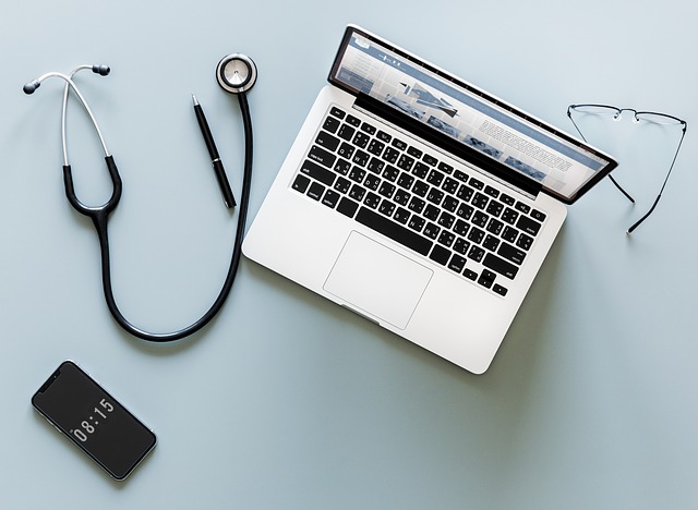 Imagen con un cuaderno en el centro, un estetoscopio a la izquierda, un teléfono celular en el frente y lentes detrás del cuaderno. La tecnología en salud necesita una mesa de ayuda humanizada.