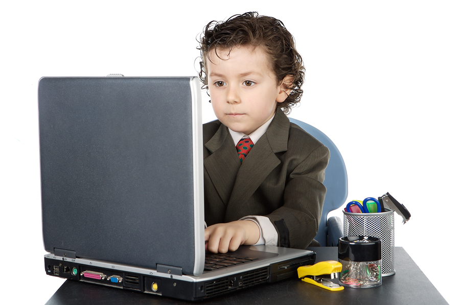 Niño vestido con traje y corbata delante de la computadora portátil. 